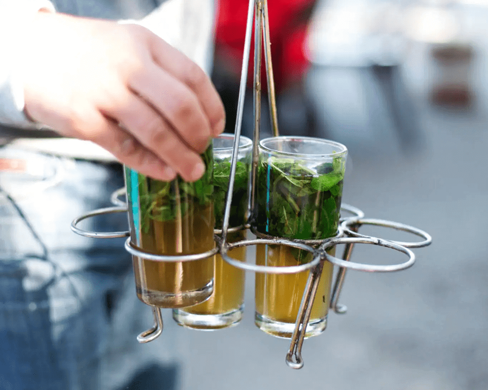 Hand holding tray with mint tea glasses.