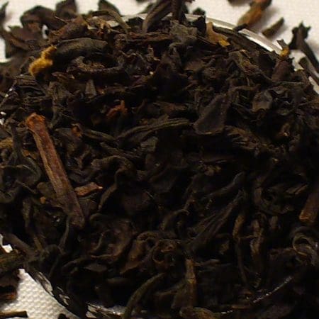 Close-up of loose black tea leaves scattered on a white surface.
