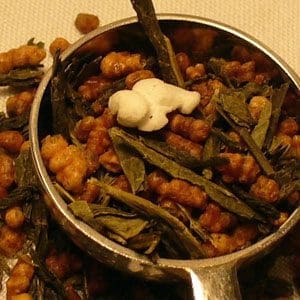 A scoop filled with cloves and dried jasmine buds on a wooden surface.