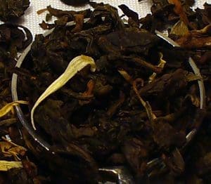 Close-up of dried dark tea leaves with a white flower petal.