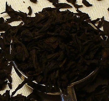 Close-up of dried black tea leaves in a glass container.